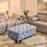 Elegancki salon z dwiema beżowymi, pikowanymi sofami M125 oraz błękitnym pikowanym pufem ustawionym centralnie, w jasnym, nowoczesnym wnętrzu.