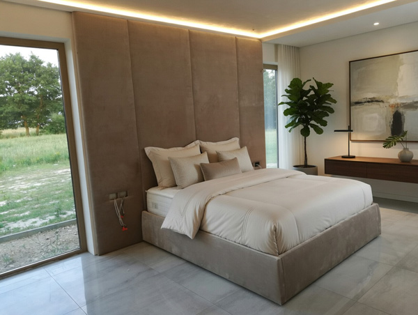 Łóżko L612 Mebel Akimo z wysokim tapicerowanym zagłówkiem, w eleganckiej sypialni z dużym oknem i minimalistycznymi dodatkami.