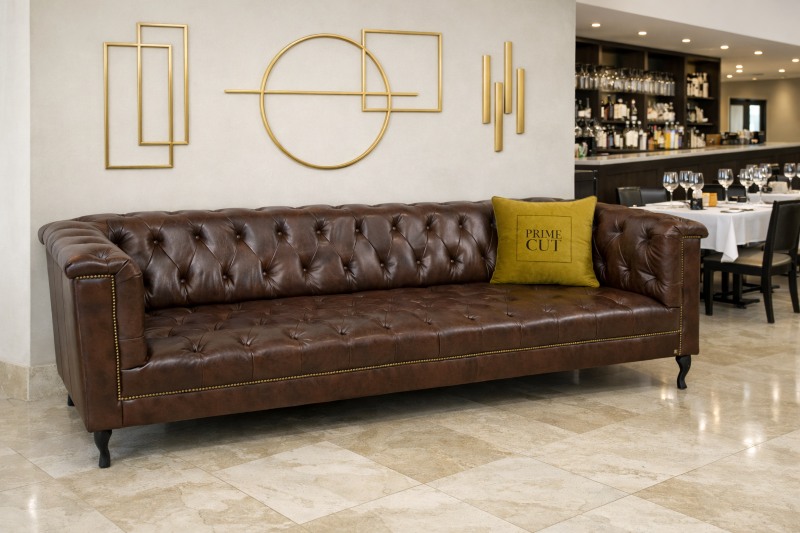 Model M161 — brązowa pikowana sofa w eleganckim wnętrzu z geometryczną złotą dekoracją i restauracyjnym tłem.