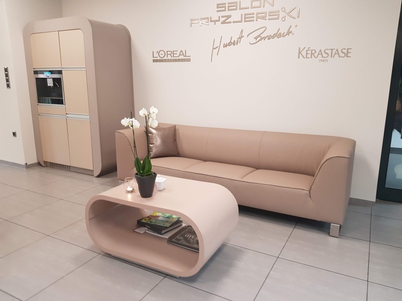 Sofa Akimo M030 w jasnej skórze w eleganckim salonie fryzjerskim z designerskim stolikiem i nowoczesnym wystrojem.